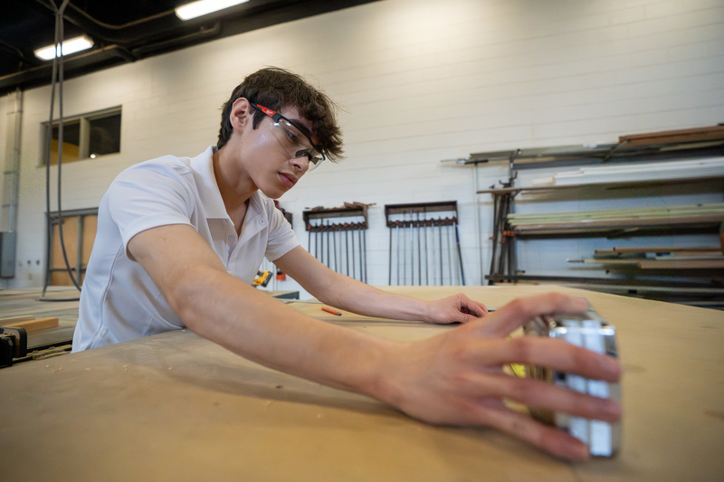teen boy using tape measure on wood
