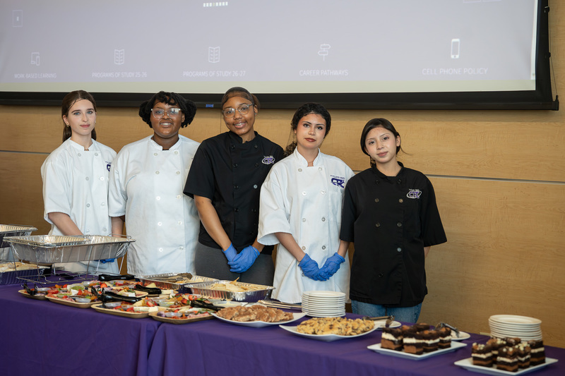 teen girls in chef coats standing behind table with food