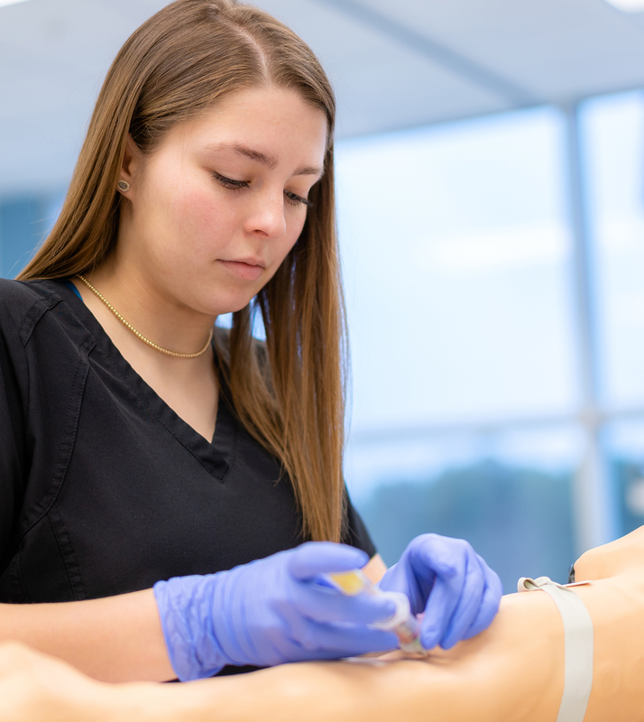 teen girl drawing blood from mannequin in health class