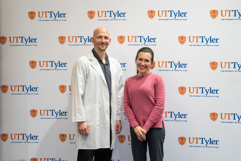 man and woman standing next to each other in front of UT Tyler sign