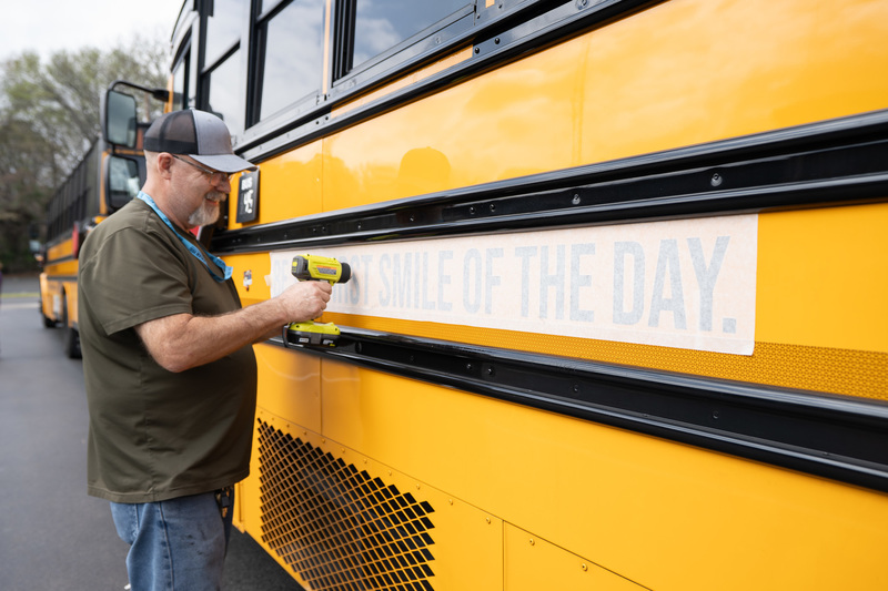 man putting stickers on side of school bus
