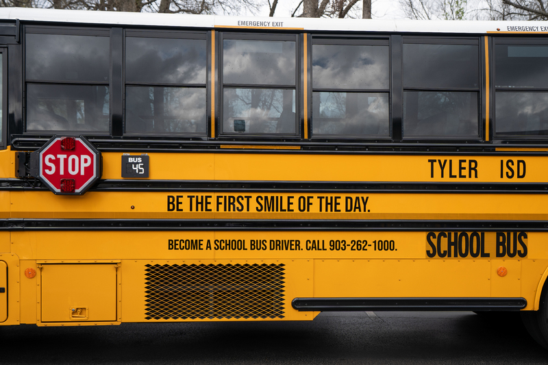 side of school bus that says, "Be the first smile of the day. Become a school bus driver. Call 903-262-1000. Tyler ISD School bus."