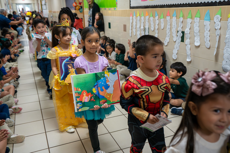 young children walking with books down school hallway