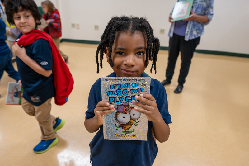 young child holding book and smiling
