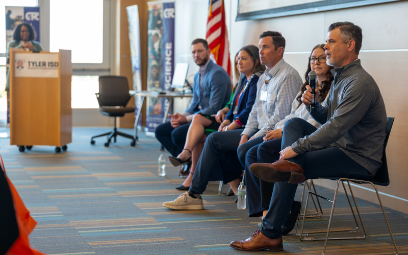 men and women sitting next to each other. one woman talking with microphone