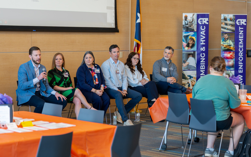 men and women sitting next to each other. one man talking with microphone
