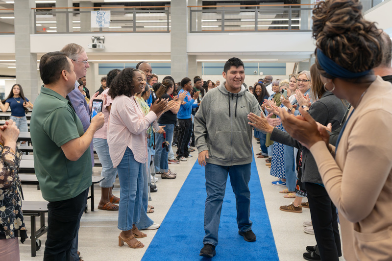 teen walking down blue carpet getting high-fives from people