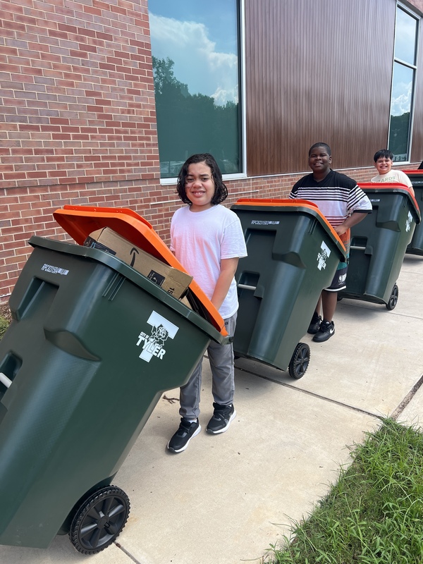 teen kids pushing green garbage cans with orange lids