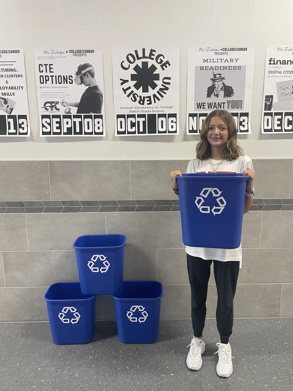 teen girl in hallway holding blue recycling bin