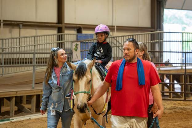 elementary age girl riding horse with two women and a man walking next to them