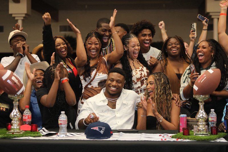 man sitting at table with men and women behind him cheering