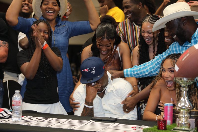 man sitting at table with men and women behind him cheering