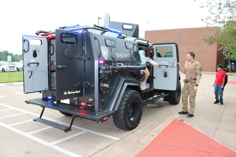 man with camo clothes holds door of SWAT vehicle as kid gets out