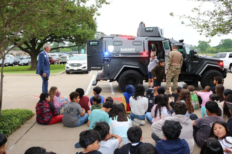 elementary age kids sitting on ground looking at SWAT vehicle