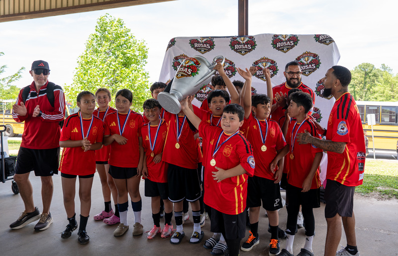 elementary age kids in red soccer jerseys holding up trophy