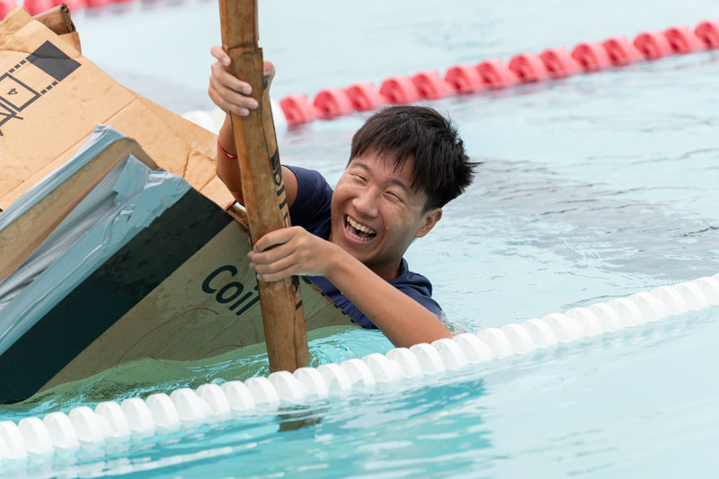 teen boy tumbling out of cardboard boat into pool