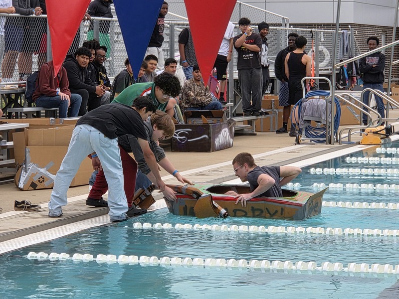teen boys reach finish line in cardboard boat in pool
