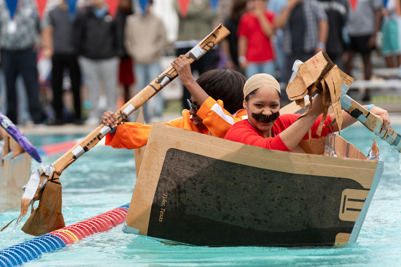 two teen girls dressed as Super Mario characters racing cardboard boat in pool