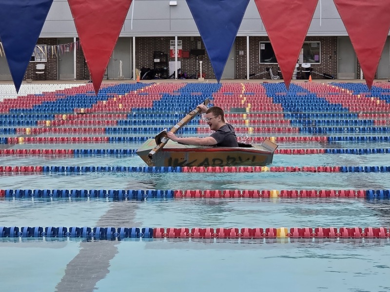 teen boy paddling cardboard boat across water in pool