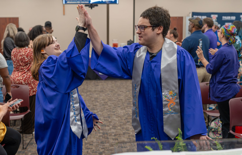 two teens in blue graduation gown high-fiving each other