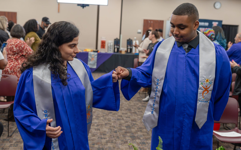 teen boy and girl in blue graduation gown fist bumping