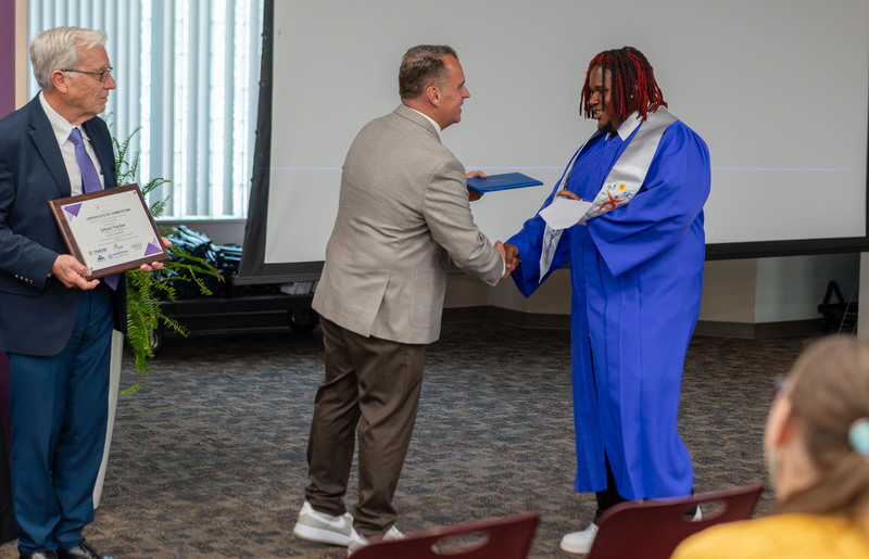 man handing diploma to teen in blue graduation gown
