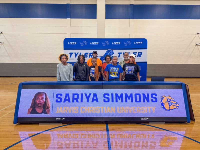 men and women standing behind table in gym with banner on front, "Sariya Simmons, Jarvis Christian University."