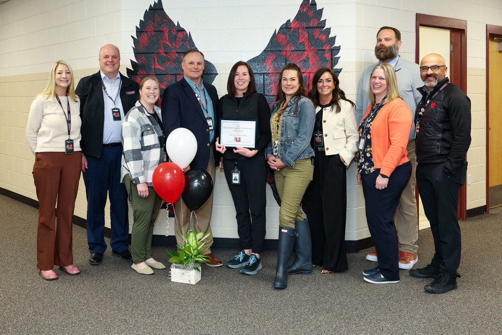 Ten school district employees pose for a photo. One of the employees in the middle holds a certificate honoring them as the Education Support Professional of the Year. 