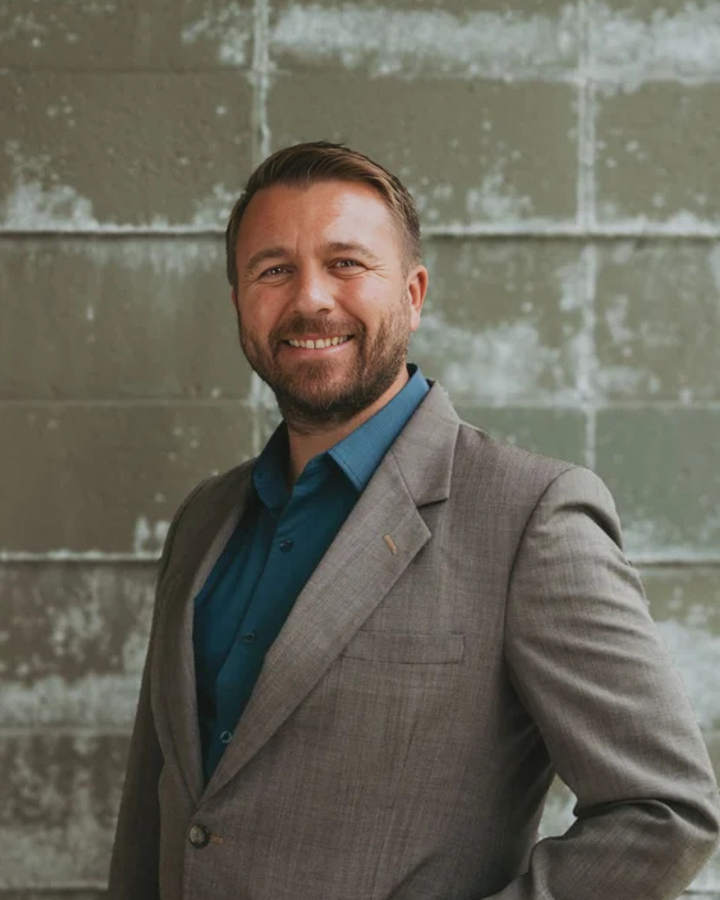 Photo of a man dressed in a dress shirt and suit jacket smiling at the camera.