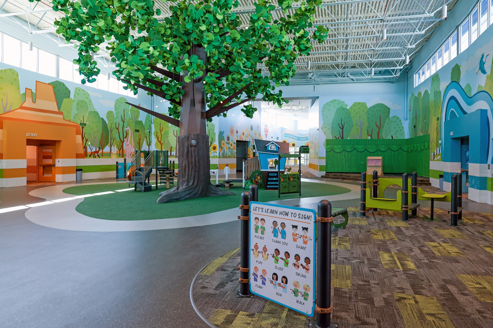 Indoor play area at Central Cove Early Learning Center with large tree play structure in the center of the space and other colorful play equipment around it.