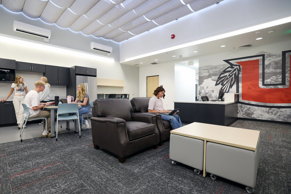 A group of high school students is pictured inside a large common space with chairs, tables, ottomans and a kitchen. A large Uintah U is on the far wall.
