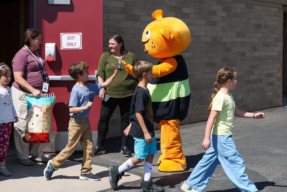 A costumed mascot of an alien gives high fives to elementary school students as they walk outside from the school cafeteria.