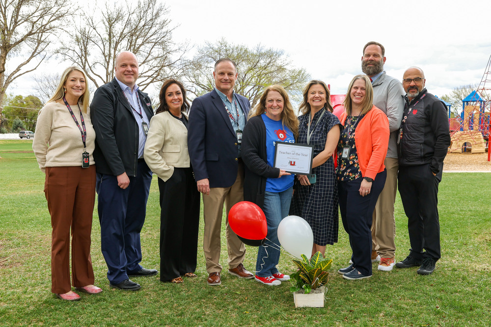Ten school district employees pose for a photo. One of the employees in the middle holds a certificate honoring them as the district's Teacher of the Year. 