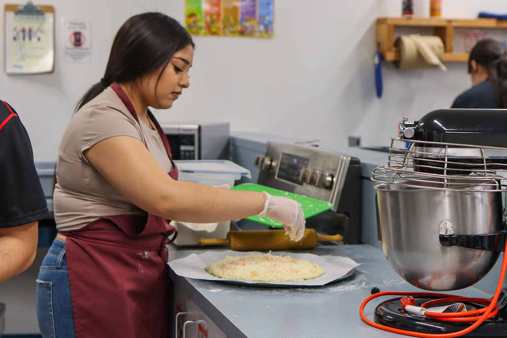 Student putting cheese on pizza