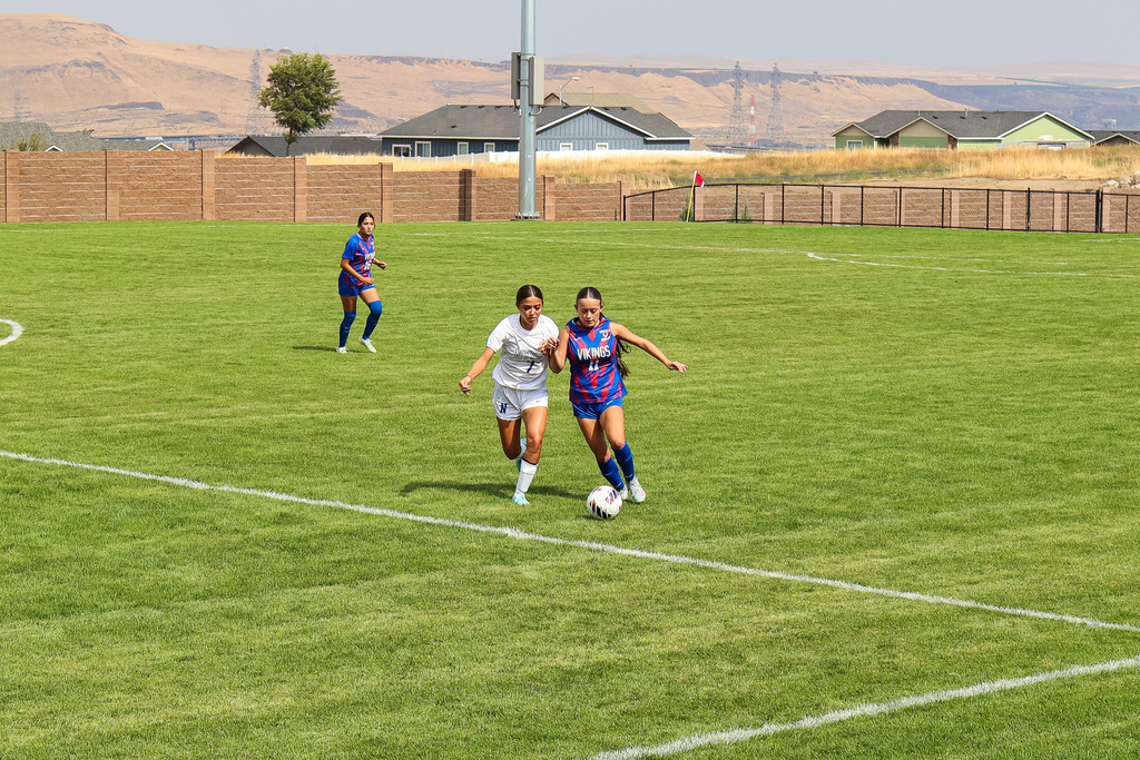 high school soccer player dribbling ball with opponent chasing after