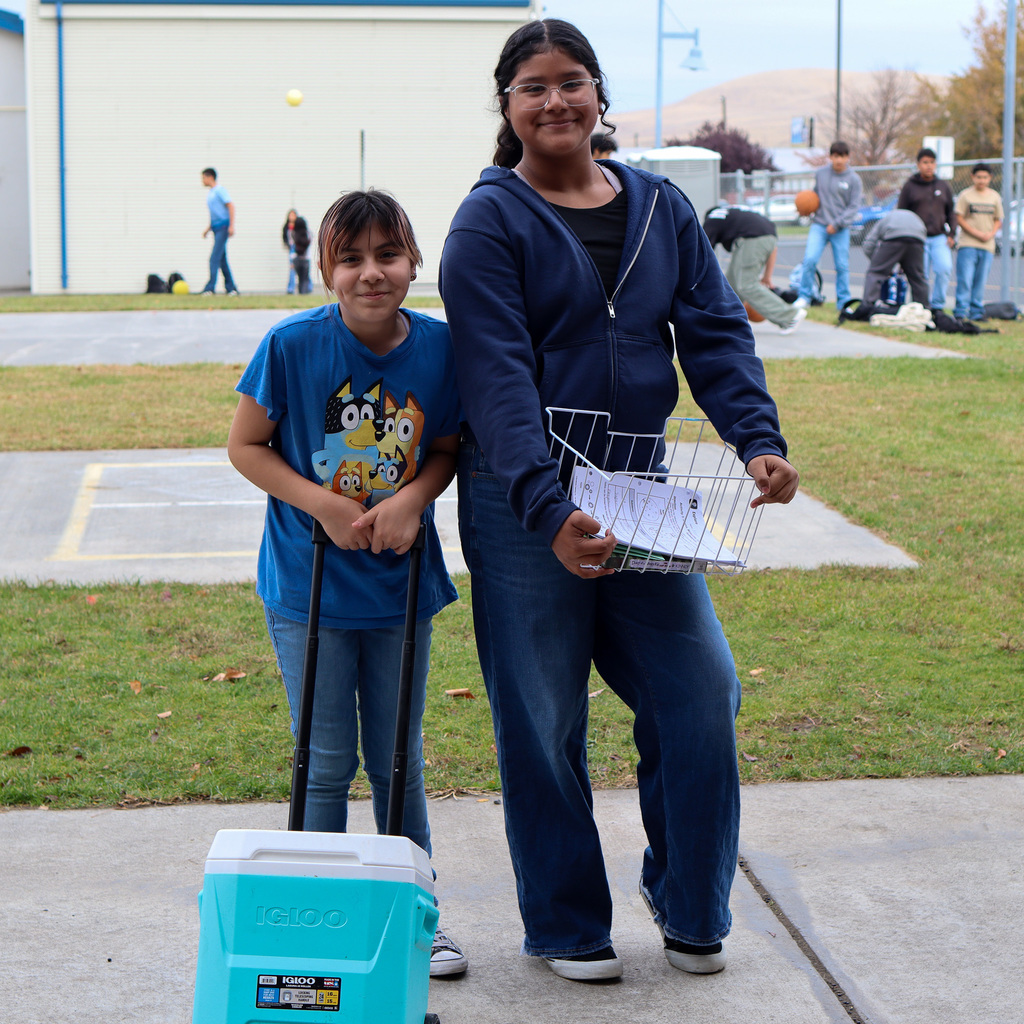Student with an ice chest with wheels and another with a paper basket