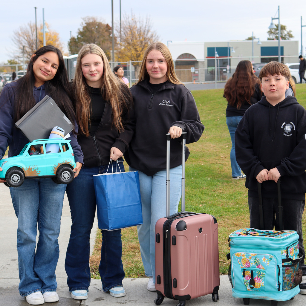 Group of students who brought anything but a backpack to school. Items include a toy car, paper bag, suite case, and ice cooler on wheels.