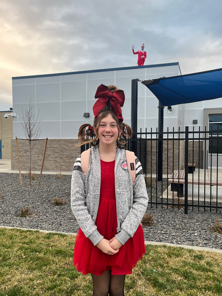 Student dressed up with the Elf on the Shelf in the background 