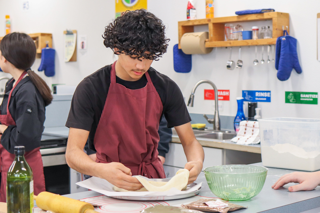 Student rolling out and forming their dough crust 