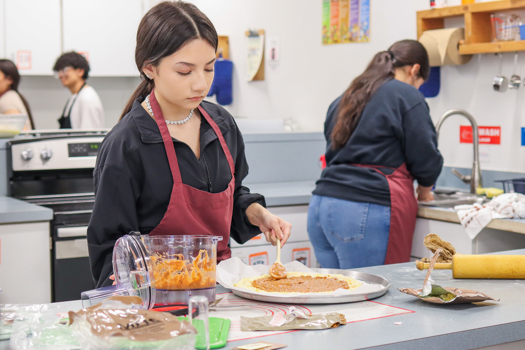 student spreading sauce on pizza 