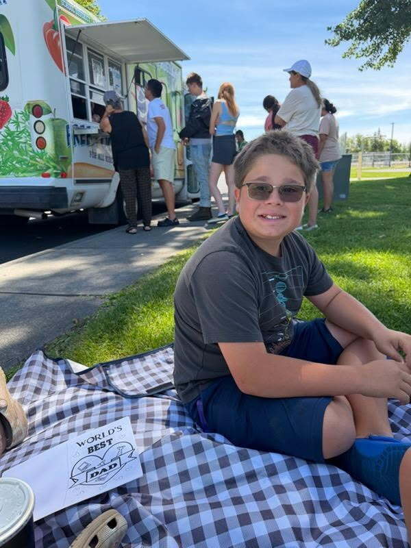 student sitting on grass in front of summer meal bus 
