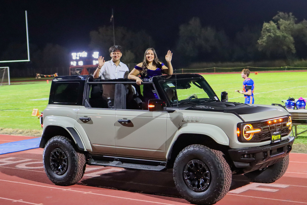 Senior homecoming royalty students waving to crowd from vehicle provided by Pierre of Hermiston
