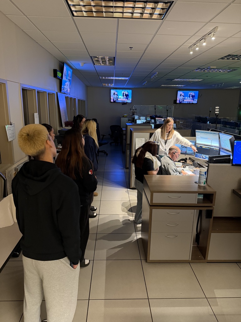 Students observe of of the communcation rooms in the Woodbury 911 Center, the lighting is low with shadows on the floor, illumination from computer monitors