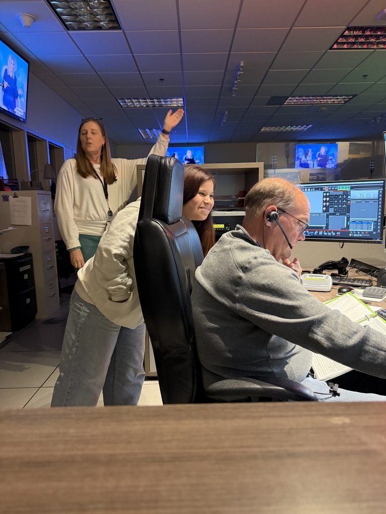 Student looks of the shoulder of one of the Communication Center operators at their station