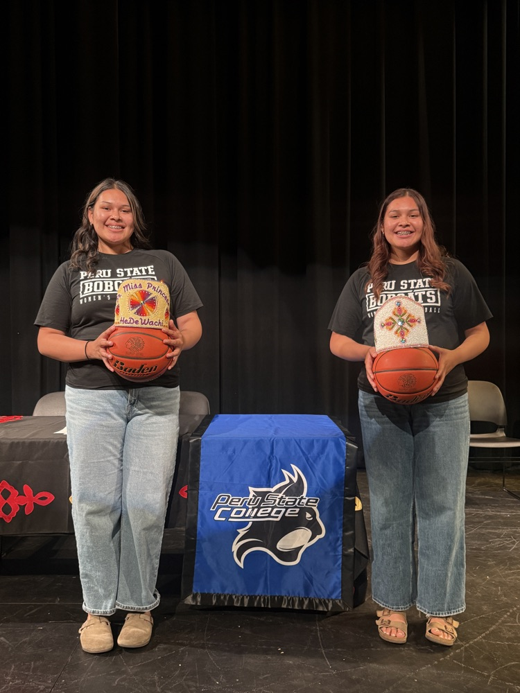 Desma and Dailene walker holding basketballs and Omaha Princess regalia in front of Peru State College banner