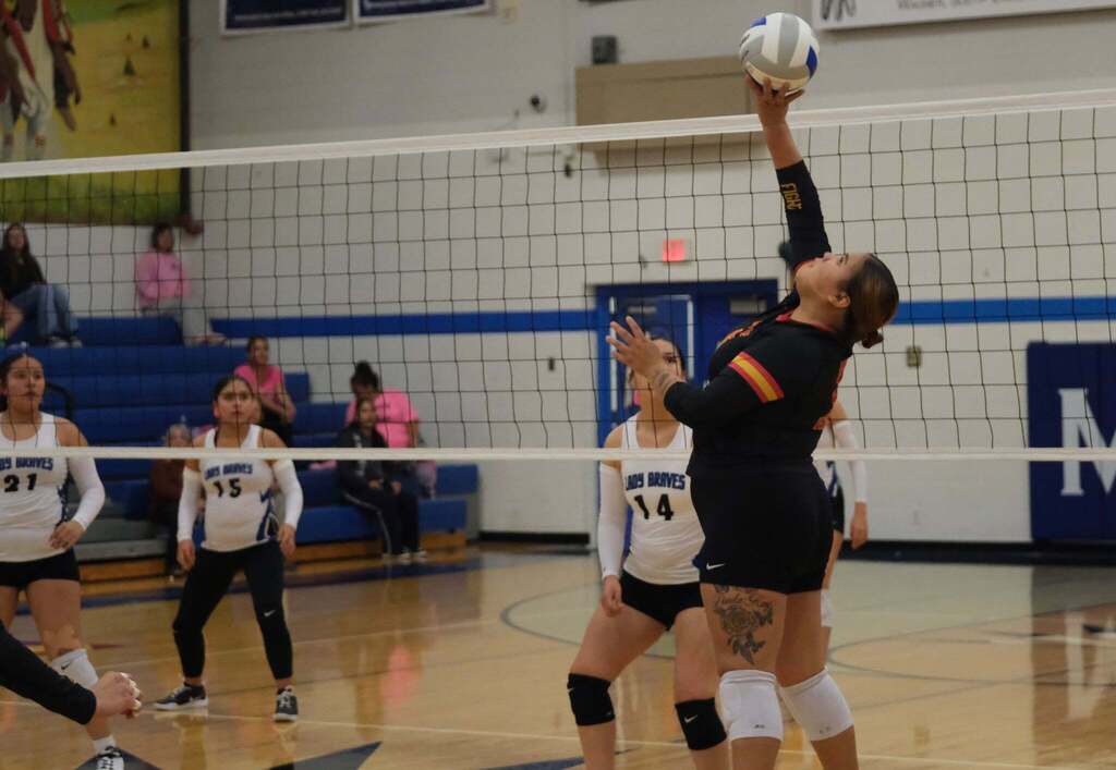 One-handed reach: A Nation player stretches one arm above the net to play the ball. Lady Braves numbers 21, 15 and 14 wait on the other side of the court.