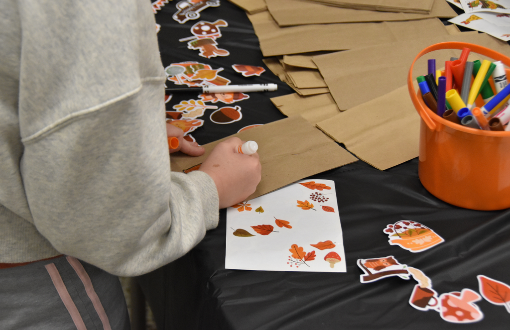 A student is drawing on a brown paper bag with orange marker