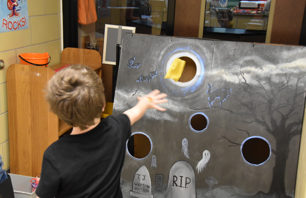 A student is throwing a bean bag into a cornhole game