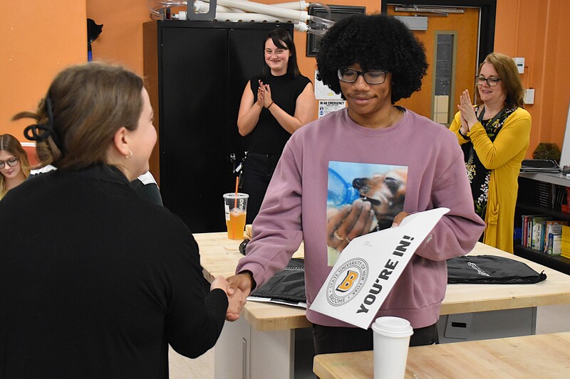Senior at Tiger Ventures shaking hands with SUNY Broome advisor while holding acceptance letter from SUNY Broome