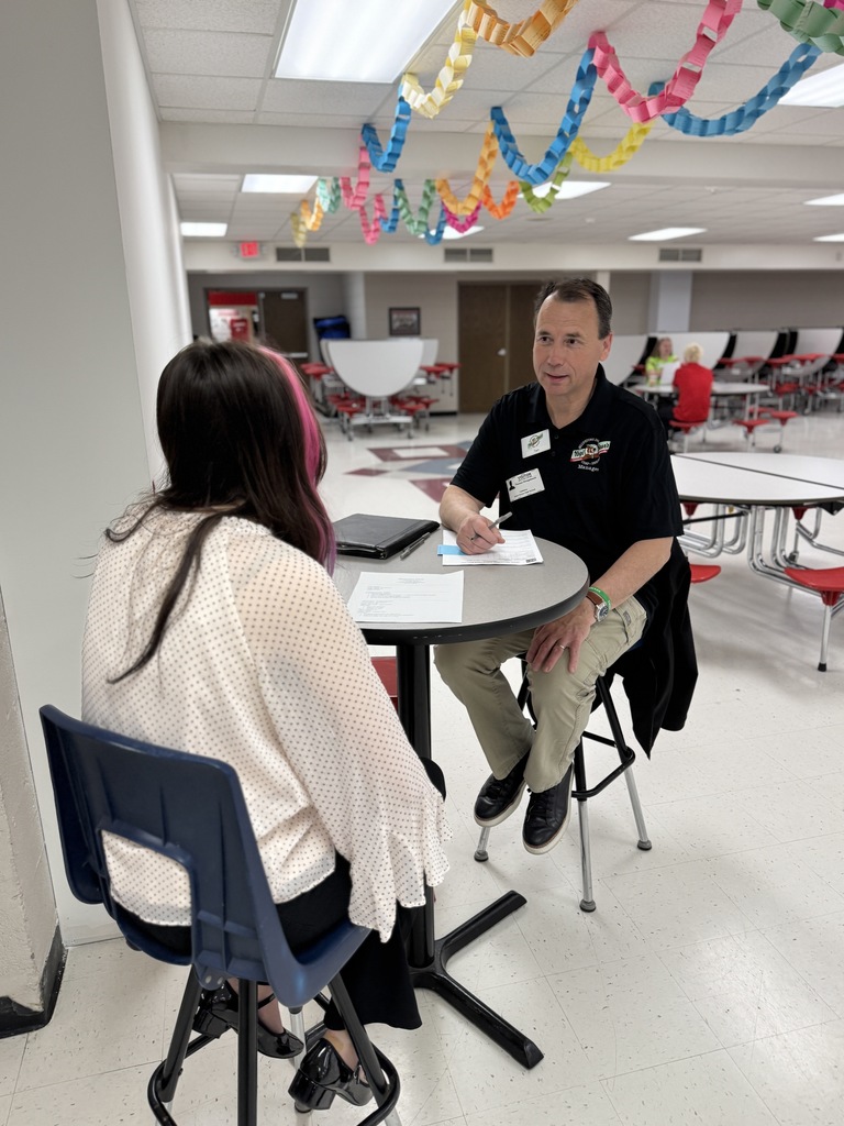 An indoor room with white floors, colorful decorations, and tables. A man and a woman sit at a table, both facing each other.